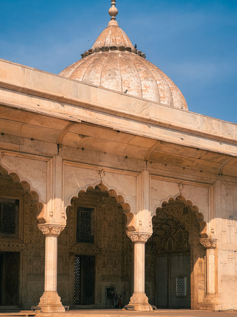 Historic sandstone structure with ornate arches and a central dome under a clear blue sky.