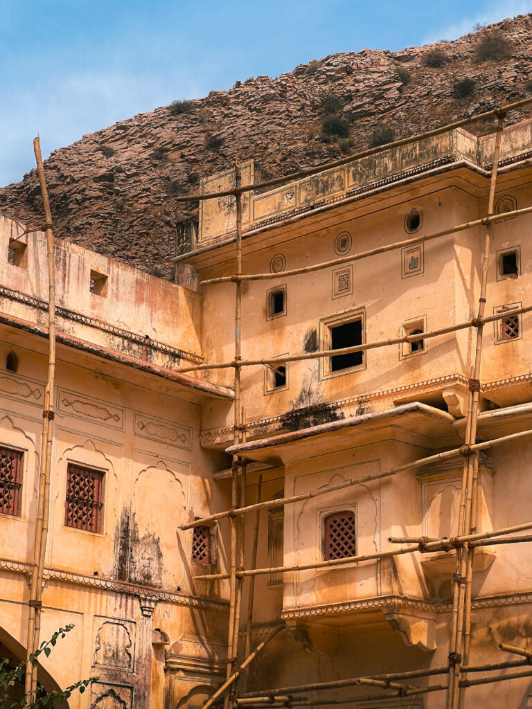 A historic yellow building under renovation with wooden scaffolding, set against a rocky hill and clear blue sky, conveying calm and preservation.