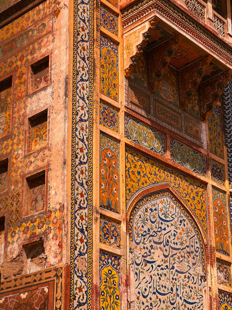Ornate building facade with intricate geometric and floral patterns in vibrant yellows, blues, and reds, reflecting traditional Islamic architecture.